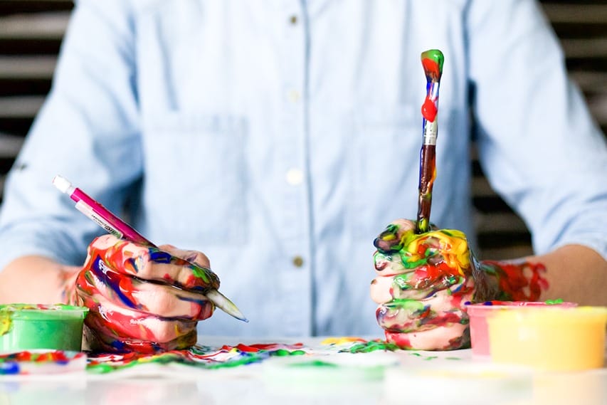 Un homme tenant des pinceaux remplis de peinture de toutes les couleurs montrant son coté créatif