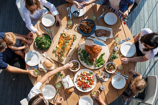 Plusieurs personnes lors d'un repas convivial avec une table remplie d'assiettes avec de la nourriture colorée.