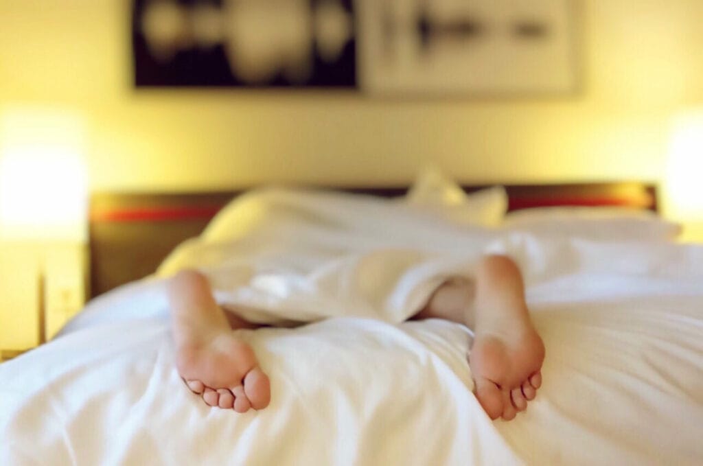 Une personne dans un lit avec un gros plan sur ses pieds qui dépassent illustrant la relation entre CBD et somnolence