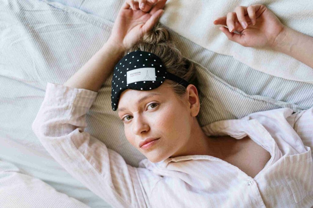 Une femme reposant paisiblement dans son lit avec un masque de sommeil sur le front, illustrant le lien entre une bonne nuit de sommeil, la perte de poids et le CBD.