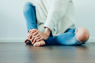 Une femme assise par terre se tenant les mains et les pieds symbolisant les eventuels effets secondaires du CBD