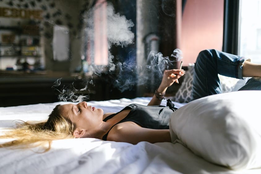 Femme allongée sur un lit fumant un joint de CBD